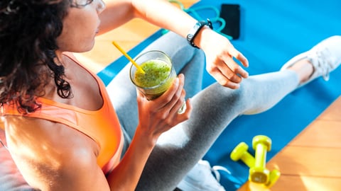 Une femme sportive regarde l'heure en buvant un smootie.