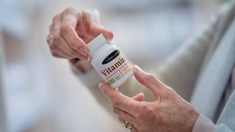 Mains d'une personne âgée tenant une boite de vitamines