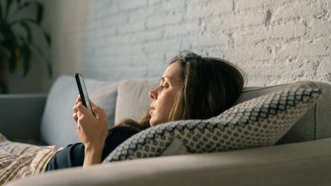 Une femme sédentaire consulte son téléphone, couchée sur un divan