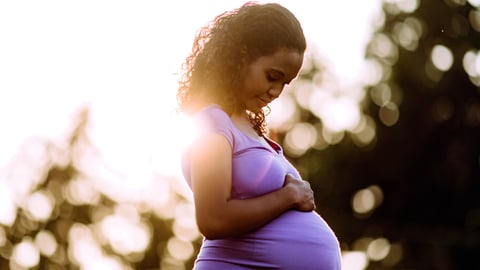 Une femme noire enceinte tient son ventre.