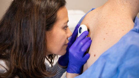 Une dermatologue inspecte la peau du dos d'un patient à l'aide d'une loupe.