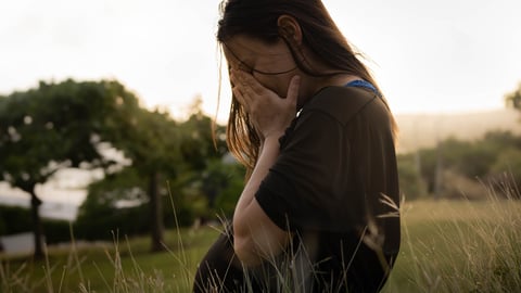 Une femme enceinte recouvre son visage de ses mains, dans un champs.