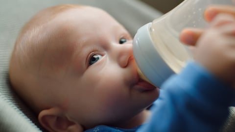 Un bébé boit au biberon, en vue rapprochée.