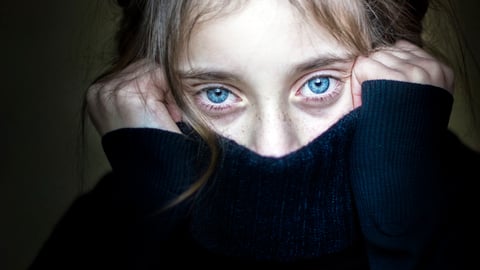 Une fillette traumatisée ou qui a peur cache une partie de son visage avec son chandail.