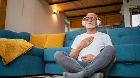 Un homme médite dans son salon avec des écouteurs sur les oreilles.