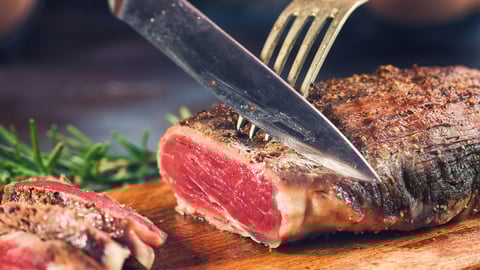 Une personne est en train de découper de la viande rouge sur une planche.