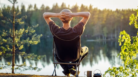 Un homme les bras croisés sur une chaise de camping dans la forêt