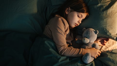 Une enfant dort dans son lit avec un toutou.