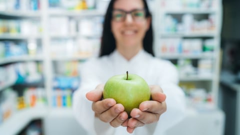 Une pharmacienne tient une pomme verte dans ses mains.