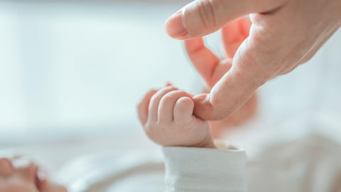 Un bébé prend le doigt d'un adulte dans sa main.