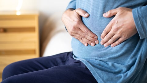 Un homme assis sur son lit souffre de crampes abdominales. 