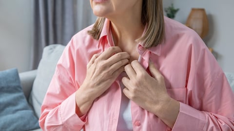 Une femme souffre de bouffées de chaleur pose ses mains sur sa poitrine en signe d'inconfort. 