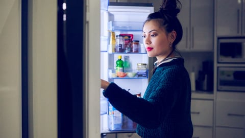 Une jeune femme regarde dans son réfrigérateur. Crédit photo: Moyo Studio  