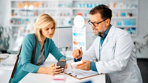 Une femme pose des questions à son pharmacien en lui montrant son téléphone. Crédit photo: Drazen Zigic/Getty Images