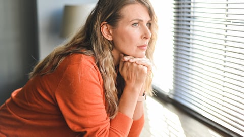 Une femme, perdue dans ses pensée, regarde à travers une fenêtre.
