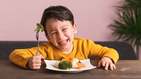 Un enfant mange ses légumes tout sourire.