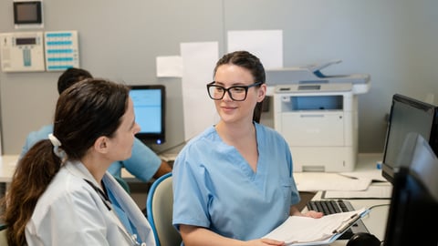 Deux médecins ou infirmières font du travail administratif à la réception en discutant.