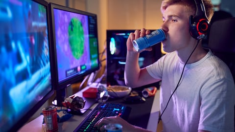 Un adolescent boit une boisson énergisante devant son ordinateur.