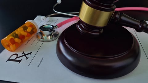Un maillet de justice posé sur une ordonnance, avec une boîte de médicaments et un stéthoscope