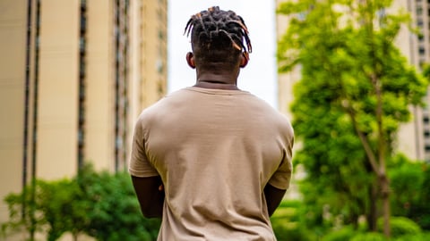Un homme jeune, musclé et noir fait face à des immeubles, de dos.