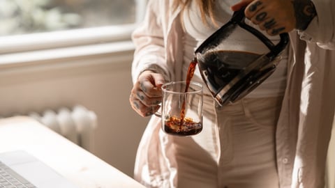Une jeune femme se sert une tasse de café filtre. 