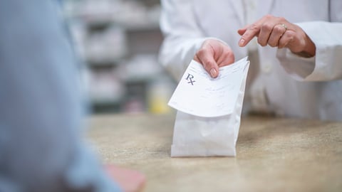Une pharmacienne remet un sac de médicaments à son client