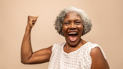 Une femme noire âgée sourit en contractant son biceps en signe de force