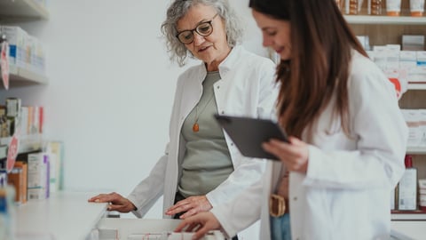 Une pharmacienne âgée et une pharmacienne plus jeune tenant une tablette examinent des médicament