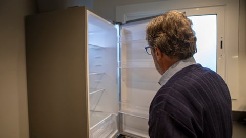 Un homme ouvre un frigo qui est vide, à son domicile.