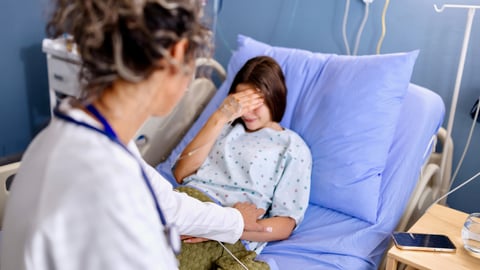 Une jeune fille pleure dans son lit d'hôpital, une soignante lui tient la main