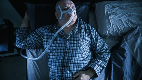 Homme en surpoids avec un masque pour l'apnée du sommeil (Photo: Getty images).
