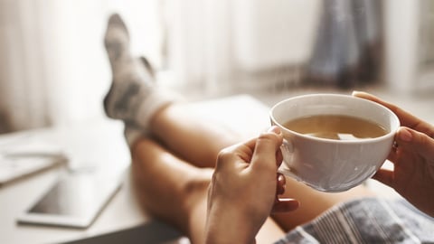 Cup of tea and chill. Woman lying on couch, holding legs on coffee table, drinking hot coffee and enjoying morning, being in dreamy and relaxed mood. Girl in oversized shirt takes break at home; Shutterstock ID 1033291948