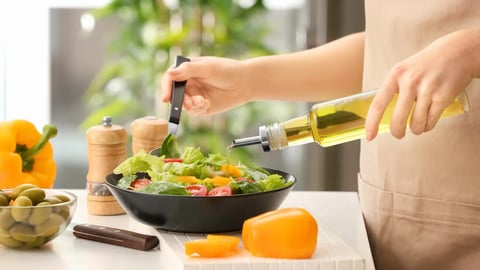 Woman dressing fresh vegetable salad with olive oil in kitchen; Shutterstock ID 1070434448