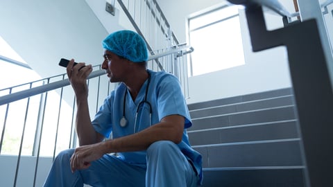 Low angle view of Caucasian male surgeon talking on mobile phone in speaker on the stairs of hospital; Shutterstock ID 1441009886