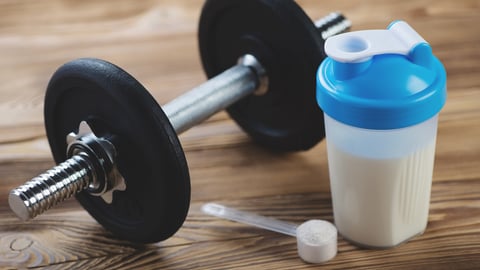 Protein shake and a dumbbell on a wooden surface; Shutterstock ID 166322195