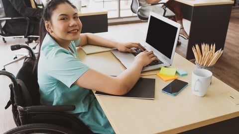 young asian disabled woman with smiling face sitting in the wheelchair and using computer to discuss project with her colleagues in the working office. disability and handicapped concept; Shutterstock ID 1770484058