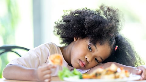 A young, curly haired African American girl sits bored looking at food. Do not want to eat food. Childhood concepts and healthy eating.; Shutterstock ID 1987719236