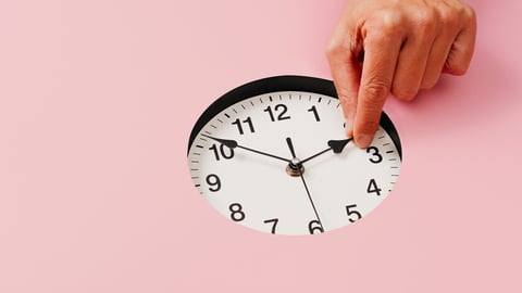 the hand of a young caucasian man sets a clock backward or forward, at the end or at the beginning of the summer, on a pink background; Shutterstock ID 2042342204