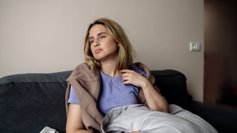 young woman with long covid syndrome - painful condition, headache, sitting on the couch at home; Shutterstock ID 2069308106