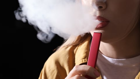 Young woman using electronic cigarette on black background, closeup; Shutterstock ID 2131869947