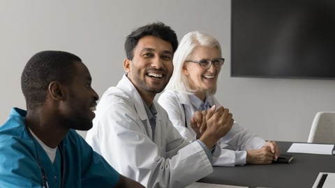 Multiethnic doctors laughing engaged in pleasant conversation seated at table in meeting room, lead discussion, share humorous or insightful comment, take part in group medical team meeting or seminar; Shutterstock ID 2504497871
