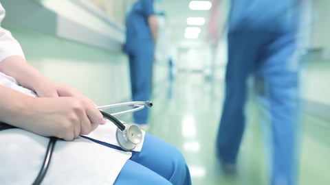 Doctor sitting alone in hospital corridor on the background of walking colleagues; Shutterstock ID 381538246