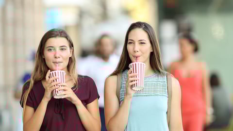 Front view portrait of two friends drinking a takeaway refreshment in the street; Shutterstock ID 688619140