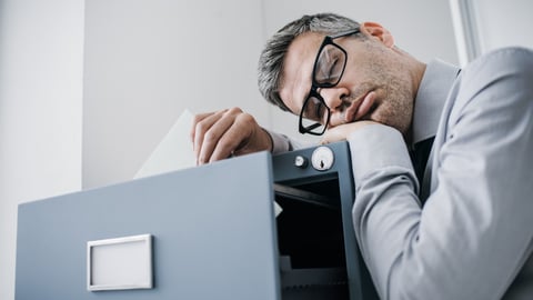 Tired lazy office worker leaning on a filing cabinet and sleeping, he is falling asleep standing up; stress, unproductivity and sleep disorders concept; Shutterstock ID 778064239
