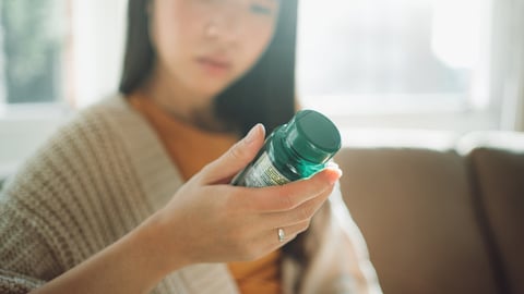 une femme lit l'étiquette d'une bouteille d'un supplément alimentaire