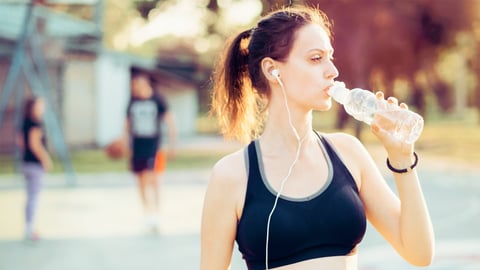 Une femme faisant du sport dans une canicule, boit de l'eau.