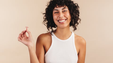 Une femme tient un stérilet / DIU en souriant