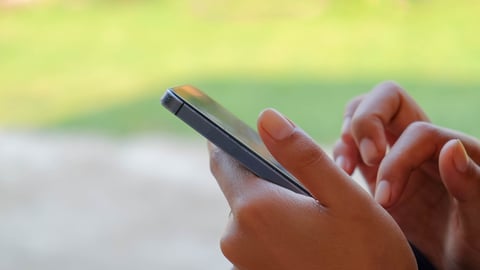 a selective focus picture of a cellphone in a woman's hand with green blur yard ; Shutterstock ID 608455982