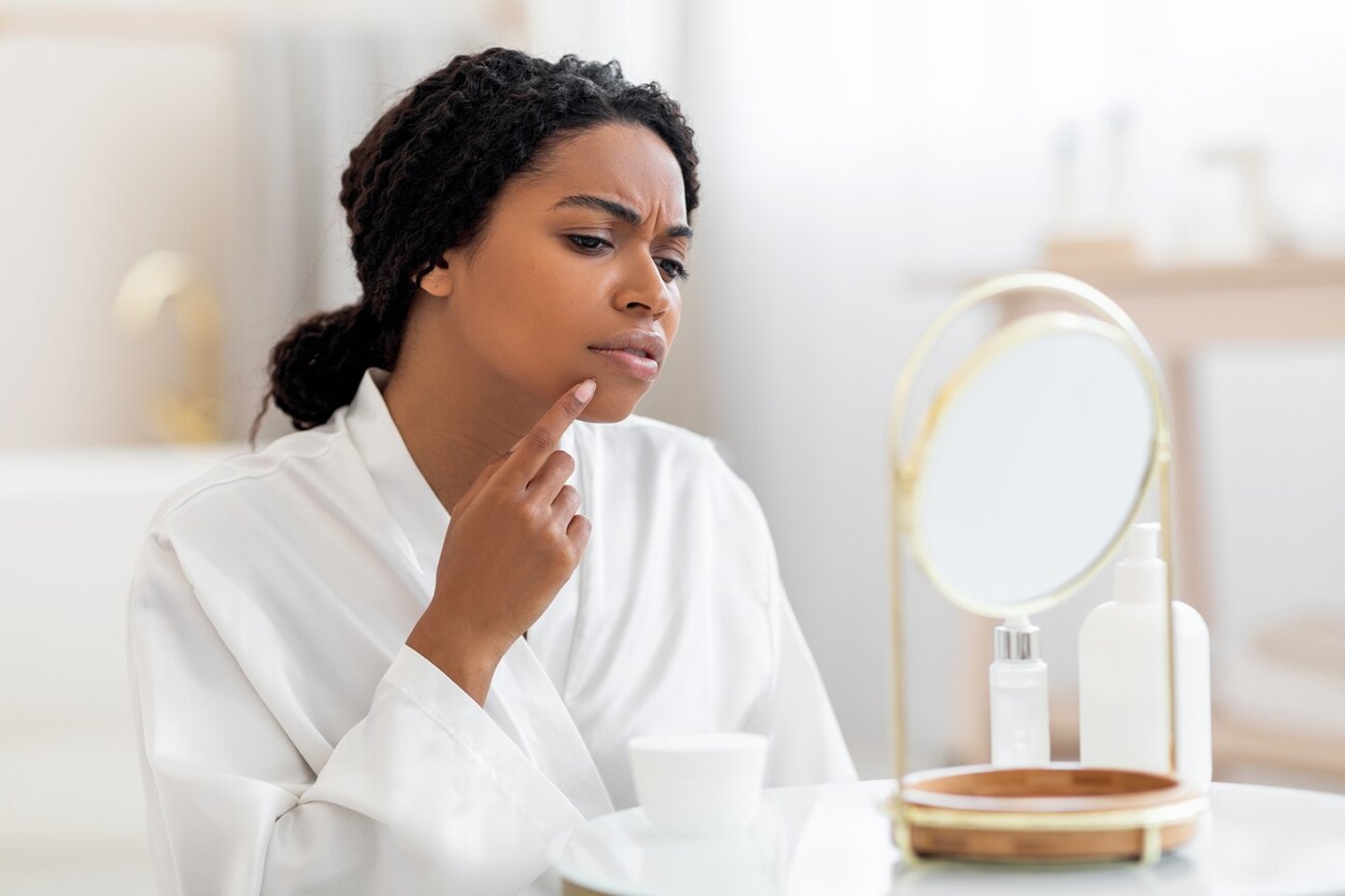 Dark-skinned woman looking at her acne in the mirror