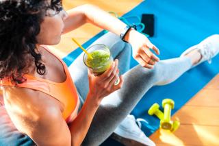 Une femme sportive regarde l'heure en buvant un smootie.